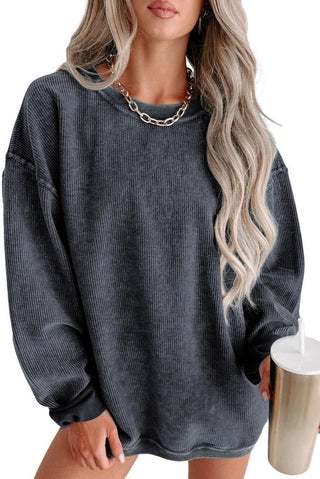 Person wearing a dark gray oversized sweater holding a metallic cup.